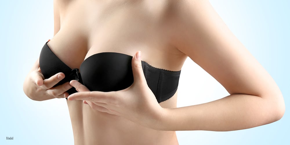 close-up of woman's breasts in a black bra against a white studio background.